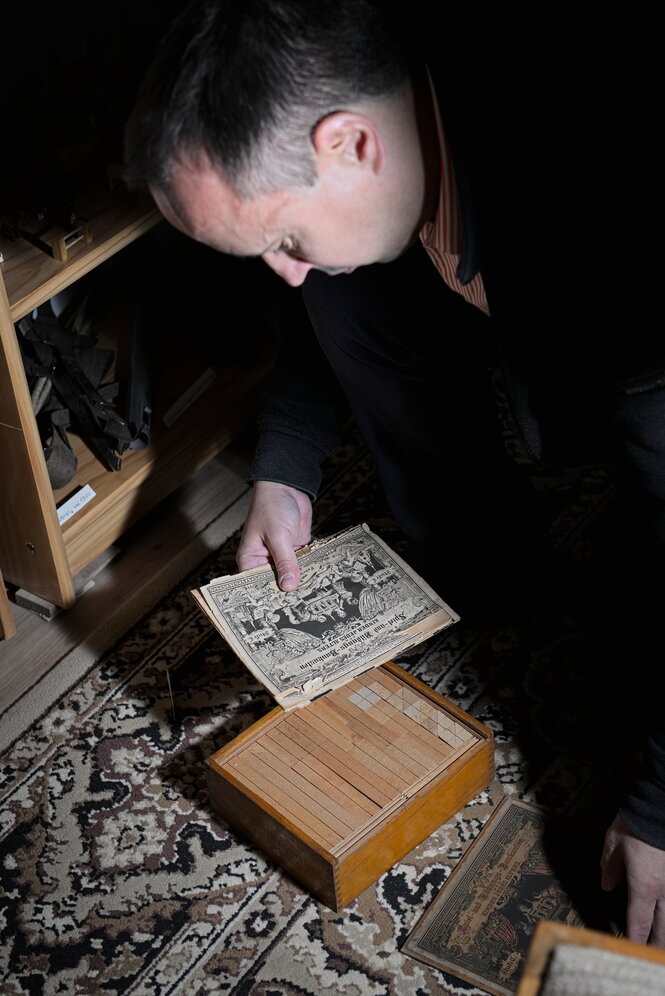 Ein mittelalter Mann schaut auf einen Holzkasten, in der Hand ein bedrucktes Blatt Papier