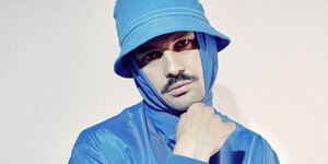 Poträtbild des Musikers Bulgarian Cartrader. Er ist ganz in Hellblau gekleidet und trägt einen Hoddie unter seinem Hut. Er hält den Hoodie mit der Hand unter dem Kinn geschlossen