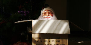 Weihnachtsmannfigur versteckt sich hinter Paket