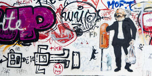 Graffiti der Kuenstler/-in Marycula mit dem Bild von Karl Marx, der etwas in einem Muelleimer sucht, in Berlin am 8. Dez