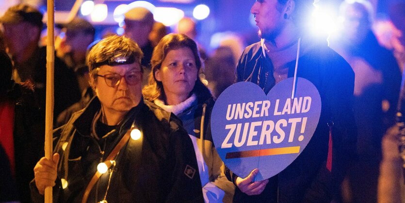 Menschenmasse, in der ein Teilnehmender ein Schild hochhält mit der Aufforderung "Unser Land zuerst"