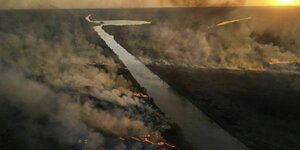 Eine Luftaufnahme von einem Fluss und Bränden mit Rauchsäulen an beiden Ufern