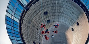 Menschen in Kletterausrüstung hängen an Seilen vor der grauen Betonwand eines Fernsehturms