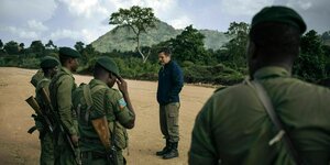 Der Direktor des Virunga Parks steht zwischen einer Gruppe von Rangern in grüner Uniform. Im Hintergrund bewaldete Hügel des Kongos