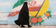 Verschleierte Frau auf der Straße vor einer iranischen Flagge