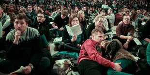 Viele junge Menschen sitzen und liegen auf dem Boden eines Veranstaltungsraums, einige singen und beten