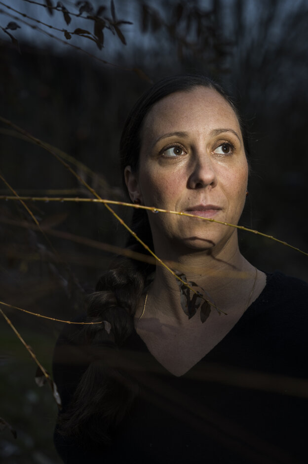 Eine junge Frau schaut nach oben, dunkler Hintergrund und Grashalme vor ihrem Gesicht