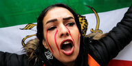 Eine Frau mit geöffnetem Mund vor einer iranischen Flagge.
