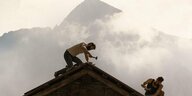 Ein Mann auf einem Dach arbeitend vor einem Alpenpanorama