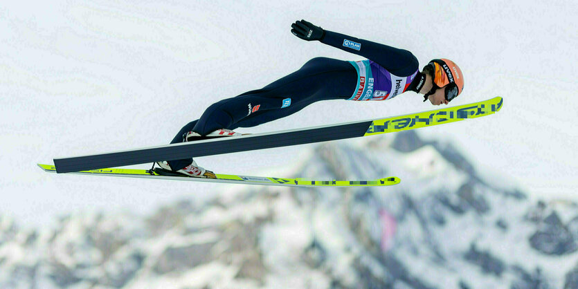 Skispringer Karl Geiger beim Flug, im Hintergrund Bergpanorama mit Schnee