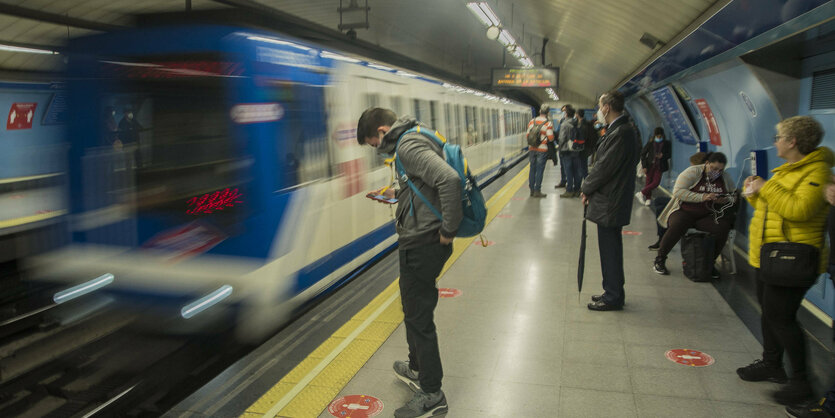 Menschen stehen am Bahngleis, während ein Zug einfährt.