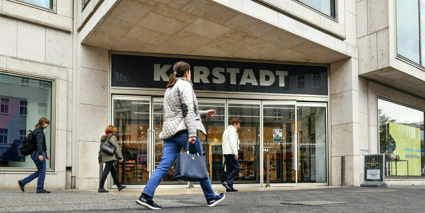 Mehrere Passanten gehen vor dem Eingang einer Karstadt-Filiale umher