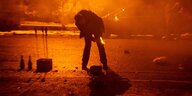 Ein Mann zündet ein Silvesterfeuerwerk an, er steht auf einer Straße im nebel