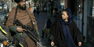 Ein Taliban-Kämpfer patrouilliert neben einer Frau in den Straßen Kabuls