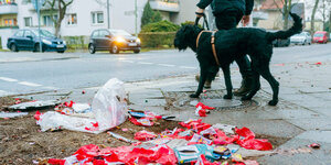 Müll liegt auf der Straße, daneben läuft ein schwarzer Hund mit seinem Herrchen vorbei
