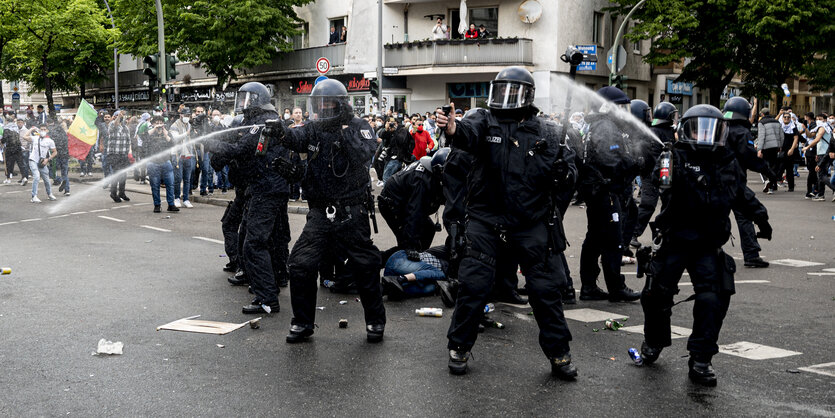 Polizisten stehen im Kreis und spürhen Pfefferspray, in der Mitte eine festgesetze Person am Boden