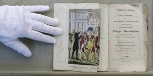 Eine Hand in weißem Handschuh hält ein altes Buch geöffnet, das von "Life" und "Amours" und "Wonderul Adventures" des "Pickpocket George Barrington" handele