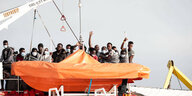 Mehrere Geflüchtete stehen hinter einem Beiboot auf der Sea Watch 3 im Hafen Pozzallo auf Sizilien