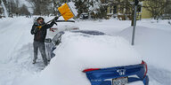 Eine Person schaufelt sein Auto von Schnee frei