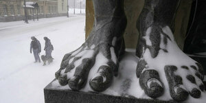 Riesige Füsse eines Atlas Denkmals in Petersburg im Schnee, dahinter 2 Nationalgardisten