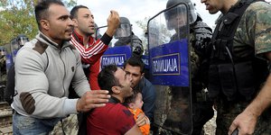 Ein Mann mit Kind kniet vor mazedonischen Polizisten