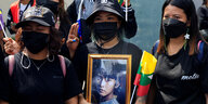Drei Demonstrantinen mit medizinischen Masken, eine hält ein Bild Aung San Suu Kyis hoch, das sie in jungen Jahren zeigt.