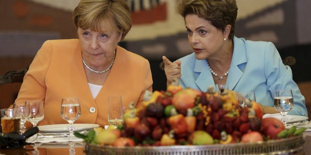 Angela Merkel und Dilma Rousseff sitzen hinter einem großen Haufen Obst