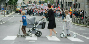 Eine Familie betrachtet beim Überqueren einer Straße einen Demonstrationszug