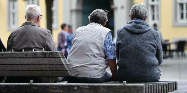 Drei ältere Menschen sitzen, mit dem Rücken zum Betrachter, auf einer Bank