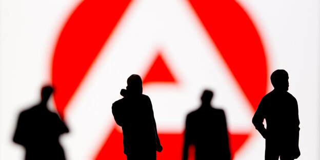 Plastic figures stand in front of a logo of the Federal Employment Agency