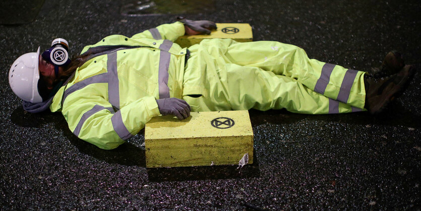 Eine Person in Schutzkleidung liegt auf einer Fahrbahn