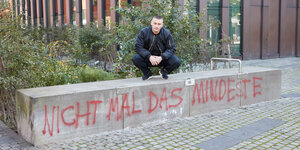Auf dem Bild ist der Hamburger Rapper Disastar auf zu sehen. Er hockt auf einer Mauer mit dem Schriftzug "nicht mal das Mindeste"