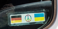Auf einem Autofenster kleben eine deutsche und eine ukrainische Fahne, zwischen ihnen ist ein Friedenszeichen