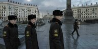 Drei junge Kadetten in Uniform im Profil. Im Hintergrund das Rund des Platzes im Zentrum von Minsk, stalinistische Architektur