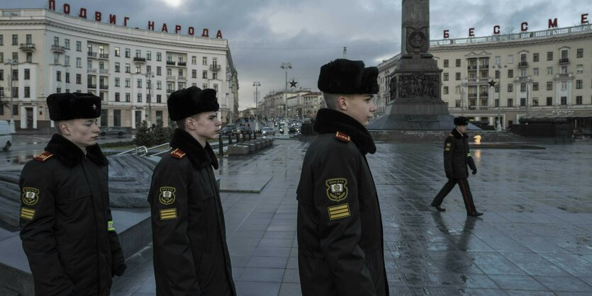 Drei junge Kadetten in Uniform im Profil. Im Hintergrund das Rund des Platzes im Zentrum von Minsk, stalinistische Architektur