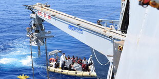 Ein kleines Boot mit Menschen nähert sich einem größeren Schiff