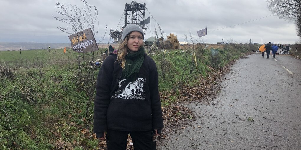 Person steht am Rande einer Straße auf dem Land. Im Hintergrund Menschen. Es ist windig und grau