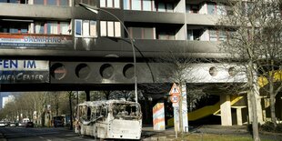 Straße mit ausgebranntem Bus, darüber Rußspuren an einem Wohnhaus