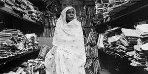 Eine indische Frau, umhüllt mit einem weißen Schleier, in einem Raum voller Hefte und Papiere