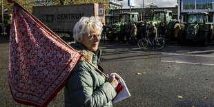 Eine Demonstrantin trägt eine Fahne, im Hintergrund stehen Trecker