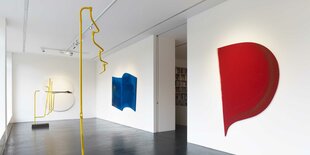 Ausstellungsansicht in die Galerie Nagel Draxler: An drei Wänden hängen Shaped Canvases von Kalin Lindena in den Farben Weiß, Blau und Rot. Zwei abstrakte Skulpturen, die aus U-Bahnhaltestangen der BVG geformt sind, stehen frei im Ausstellungsraum