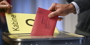 Das Foto zeigt eine Hand mit einem Wahlumschlag über einer Wahlurne.
