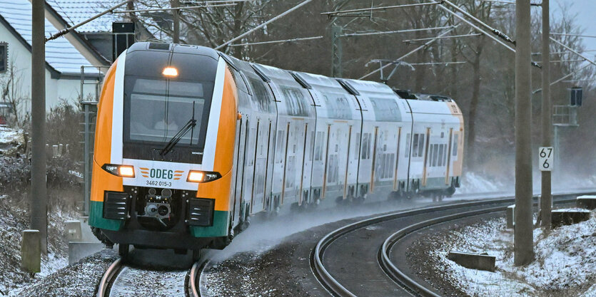 Ein Zug von dem Betreiber Odeg fährt auf verschneiten Bahngleisen um eine Kurve