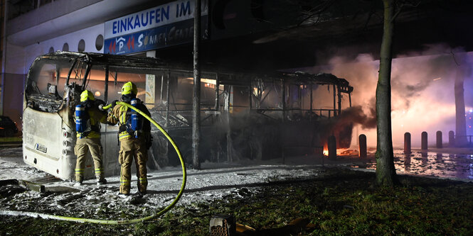 Feuerwehrmänner löschen an der Sonnenallee in Berlin einen Reisebus, der nach Mitternacht an Silvester von Unbekannten angezündet worden war