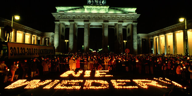 Das Bild zeigt eine Versammlung zum Gedenken an die Machtergreifung der Nationalsozialisten vor dem Brandenburger Tor im Jahre 1993.. Zu sehen ist außerdem eine Lichterkette mit den Worten „Nie wieder“.