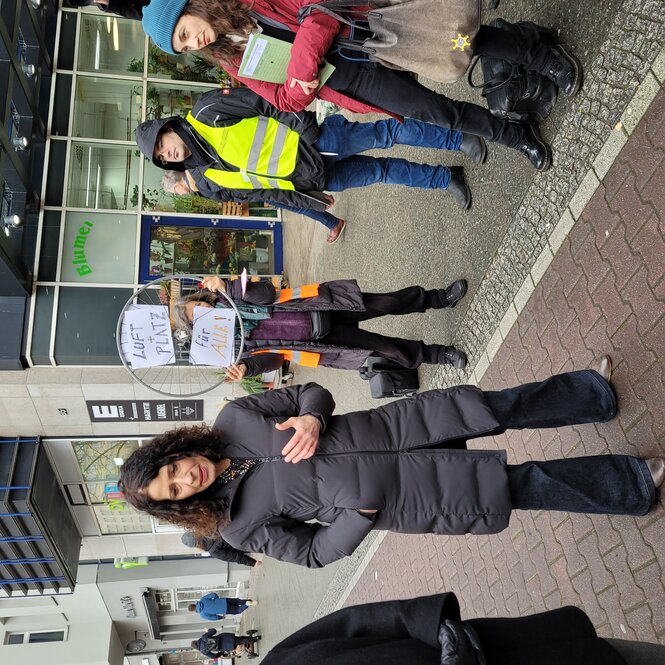 Bettina Jarasch spricht auf einem Termin, im Hintergrund Protestierer