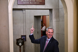 Kevin McCarthy zeigt mit einem Finge nach oben zu dem Schild, das über einem Durchgang hängt und seinen Namen und Titel trägt