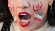 Ein Frauenkopf, der nur bis über der Nasenspitze zu sehen ist. Der Mund ist geöffnet. Auf den Wangen: die iranische Fahne und Schriftzeichen