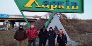 Fünf Menschen stehen vor einem Ortsschild auf dem in ukrainischer Schrift „Charkiw“ steht