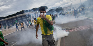 Straßenszene in Brasilia mit Rauchschwaden, im Fokus ein Mann in gelbgrün gekleidet, mit Atemmaske